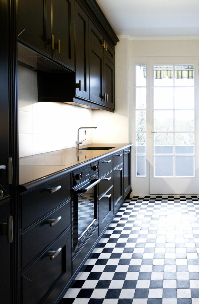 Cuisine sur mesure en bois laqué noir et plan de travail en granit clair avec carrelage en damier noir et blanc